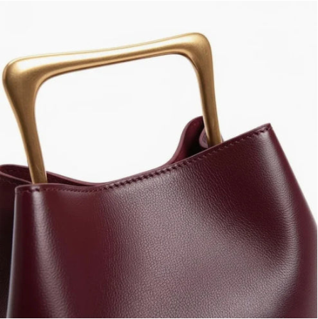 Close up burgundy ayla handbag with gold handle on a white background