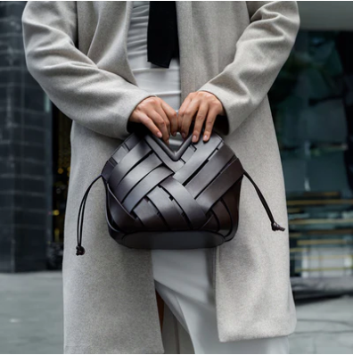 Person holding a woven handbag in an urban setting